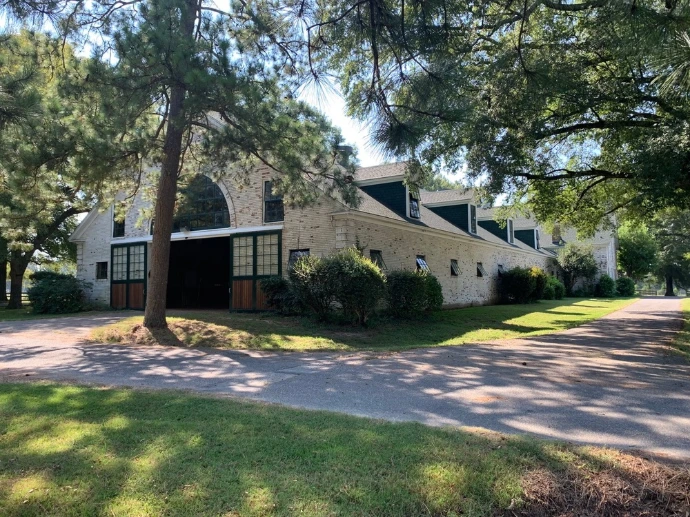Stone and cream painted barn with multiple cupolas and covered walkway featuring arched stall openings