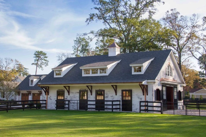 White barn with dark roof, black shutters, dormers and X-pattern stall doors on green lawn