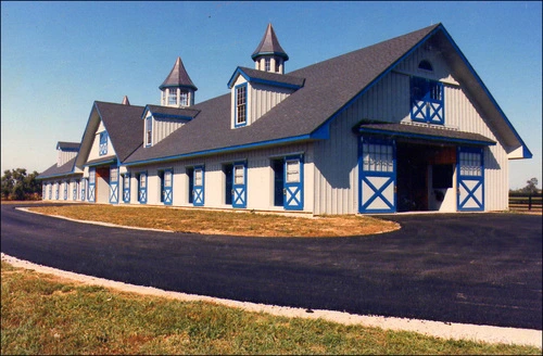 Large blue barn with cream trim, X-pattern stall doors and dual cupolas on gambrel roof