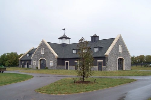 Gray stone barn with steep rooflines, cupolas and circular driveway on green campus
