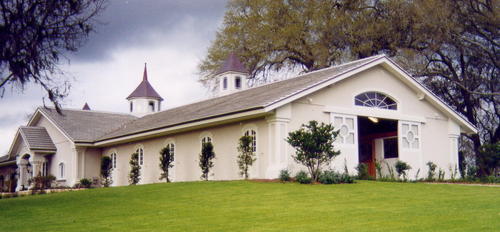 White barn with cupola, arched entrance and covered walkway in landscaped setting