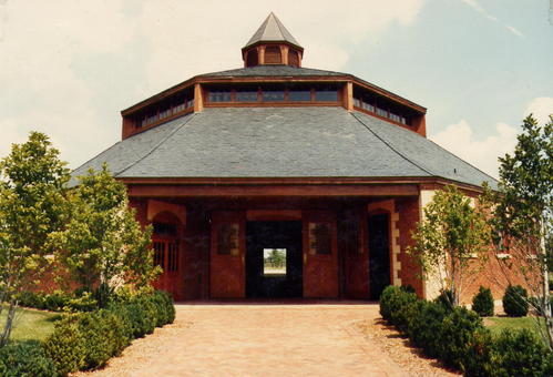 Red brick octagonal barn with cupola, gray roof and large arched wooden door opening