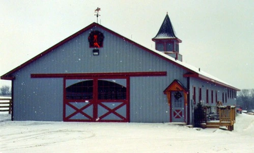 Gray barn with red trim, cupola and X-pattern doors in winter snow setting