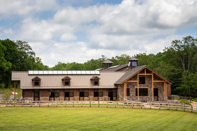 Timber-frame barn with natural wood siding, stone foundation and wood rail fencing