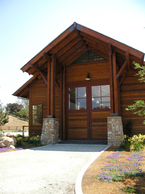 Natural wood barn with timber-frame overhang, stone pillars and glass panel doors