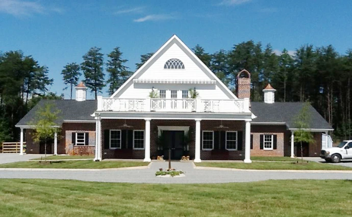 White barn with dark roof, black shutters, cupola and arched center entrance with parked vehicles