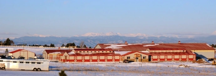 Long red metal roof barn complex with cream walls and mountain range visible in background