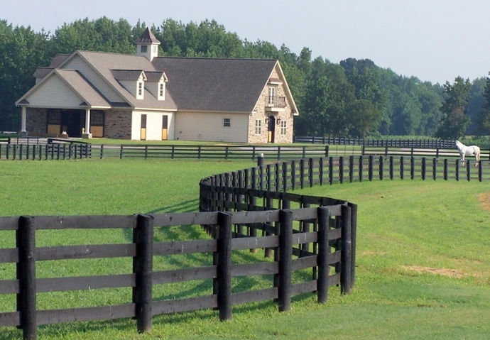 White barn with dark roof, cupola and black board fencing in rolling green pasture