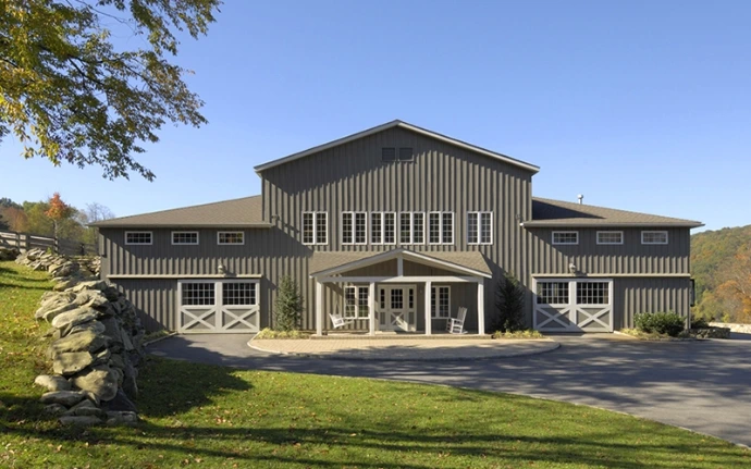 Gray metal barn with large glass panel windows and doors on two levels in hillside setting