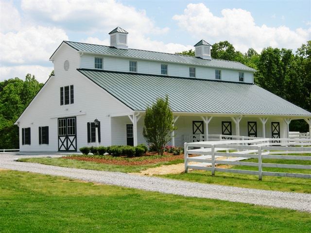 White barn with gray metal roof, X-pattern stall doors and white board fencing
