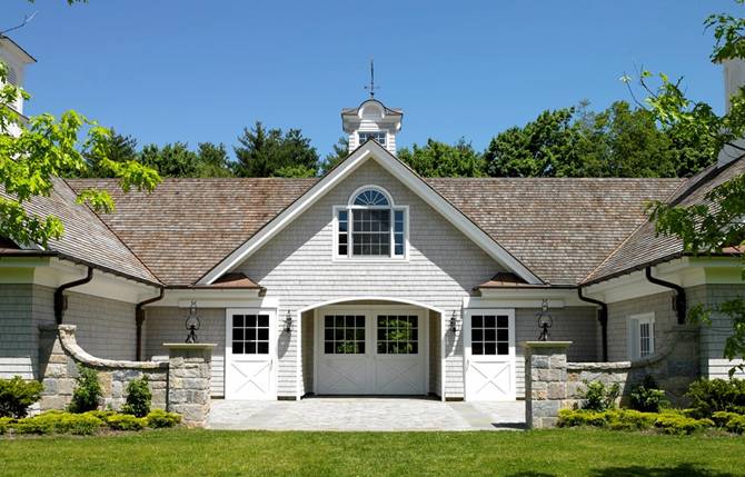 White barn with gray stone pillars, dark shutters and arched overhead door openings