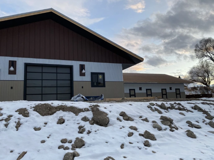 Modern white barn with dark brown roof and large glass panel overhead doors in winter