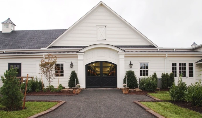 White barn with dark roof, symmetrical design and arched entrance with landscaping
