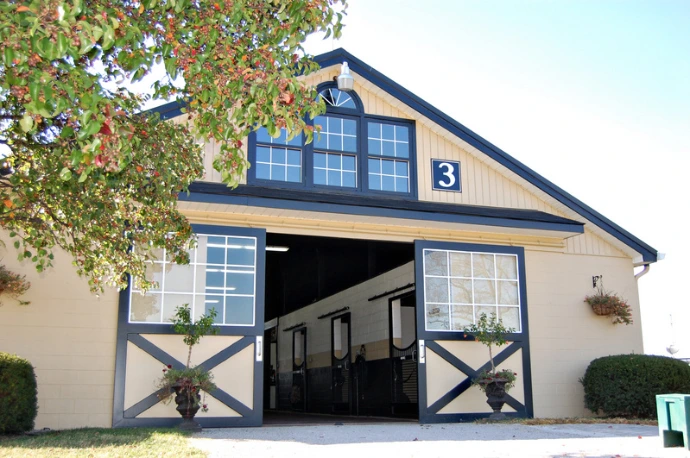 Cream barn with blue roof, large arched entrance and X-pattern door in gable
