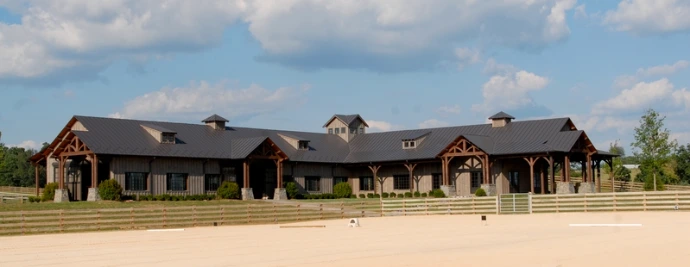 Brown barn with multiple dormers and cupolas on dark roof in rural setting
