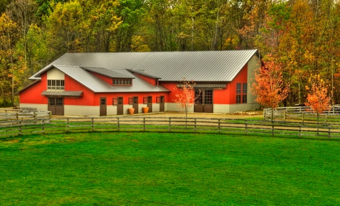 Red barn with gray metal roof and multiple X-pattern stall doors in autumn setting