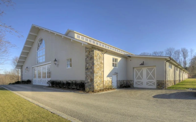 White stucco barn with stone accents, arched overhead doors and green lawn