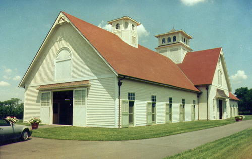 Cream barn with red terracotta roof, arched window in gable and covered porch area