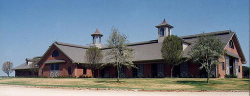 Red brick barn complex with brown roofs, multiple cupolas and rolling green landscape