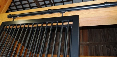 Maintenance-Free Roundrail Track: Close-up of black metal sliding door track system with vertical bars mounted on natural wood header showing completely round track design