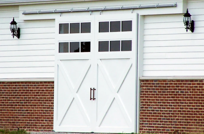 White barn with carriage-style doors featuring X-pattern and multi-pane windows between brick accents