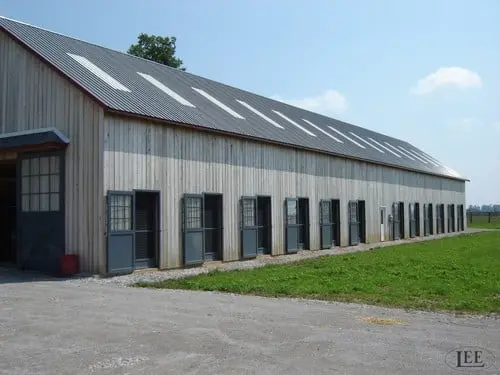 What's the Difference Section Image: Long gray vertical metal barn with multiple skylights on roof and row of stall door openings along side in green pasture setting